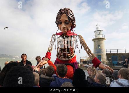 Die kleine Amal, eine 3.5 Meter große Marionette eines neunjährigen syrischen Mädchens, wird von Kindern der St. Mary's Primary Academy begrüßt, als sie in Folkestone, Kent, als Teil des "The Walk" der Handspring Puppet Company ankommt. Bilddatum: Dienstag, 19. Oktober 2021. Stockfoto