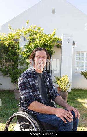 Porträt eines behinderten kaukasischen Mannes, der auf einem Rollstuhl sitzt und im Garten lächelt Stockfoto