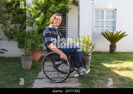 Porträt eines behinderten kaukasischen Mannes, der auf einem Rollstuhl sitzt und im Garten lächelt Stockfoto