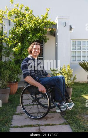 Porträt eines behinderten kaukasischen Mannes, der auf einem Rollstuhl sitzt und im Garten lächelt Stockfoto