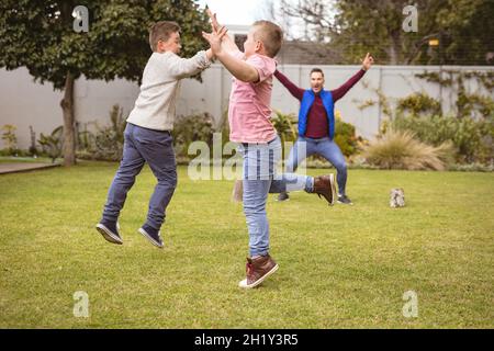 Kaukasischer Vater und zwei Söhne spielen gemeinsam im Garten Fußball Stockfoto