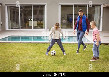 Kaukasischer Vater und zwei Söhne spielen gemeinsam im Garten Fußball Stockfoto