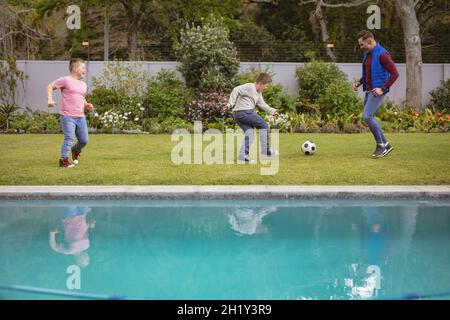 Kaukasischer Vater und zwei Söhne spielen gemeinsam im Garten Fußball Stockfoto