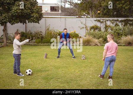 Kaukasischer Vater und zwei Söhne spielen gemeinsam im Garten Fußball Stockfoto
