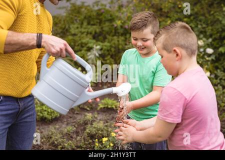 Kaukasischer Vater gießt Wasser, während zwei Söhne sich im Garten die Hände waschen Stockfoto