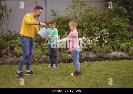Kaukasischer Vater gießt Wasser, während zwei Söhne sich im Garten die Hände waschen Stockfoto