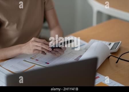 Geschäftsfrau, die Finanzdaten aus einem monatlichen Papierbericht mit Smartphone und Laptop analysiert Stockfoto