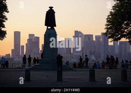 Menschen, die den Sonnenuntergang im Greenwich Park mit den Wolkenkratzern von Canary Wharf im Hintergrund beobachten, London, England, Großbritannien Stockfoto