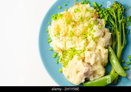 Zarte Stücke geräucherter Schellfisch und pollock in einer cremigen Käsesoße saßen unter buttriger Maische, serviert mit grünem Gemüse, klassische englische Mahlzeit Stockfoto