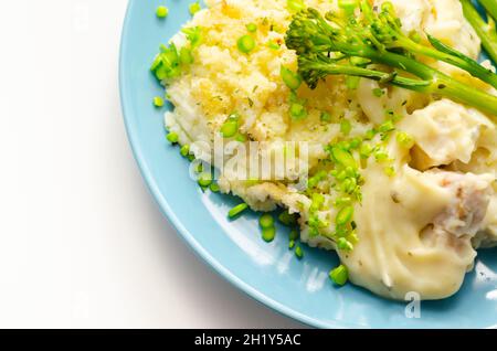 Zarte Stücke geräucherter Schellfisch und pollock in einer cremigen Käsesoße saßen unter buttriger Maische, serviert mit grünem Gemüse, klassische englische Mahlzeit Stockfoto