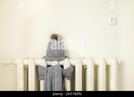 Vintage Heizkörper mit Wolle gestrickter Wintermütze und Schal. Die Strom- und Gasrechnung steigt, europäisches Energiekrisenkonzept. Stockfoto