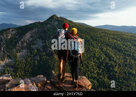 Ein glückliches Paar in den Bergen bewundert die schöne Aussicht. Ein Mann und eine Frau mit Rucksäcken auf dem Berg bewundern den Panoramablick. Reisende
