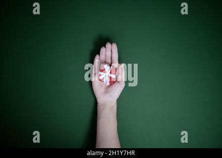 Eine kleine, rot glänzende Schachtel liegt in der Handfläche einer Frau auf einem grünen Hintergrund. Draufsicht Stockfoto