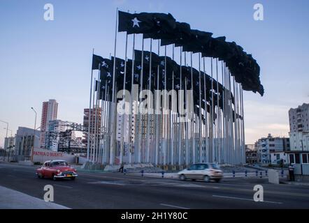 138 schwarze Flaggen mit weißen Sternen, bekannt als die 'Wall of Flags' auf der Plaza de la Dignidad, mit typisch amerikanischem Oldtimer, der vorne vorbeifährt. Kuba. Stockfoto