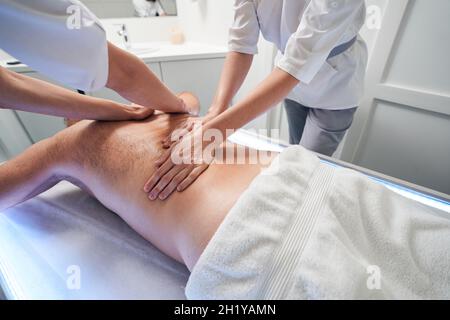 Zwei Masseuse massieren den Mann im Wellnesscenter zurück Stockfoto