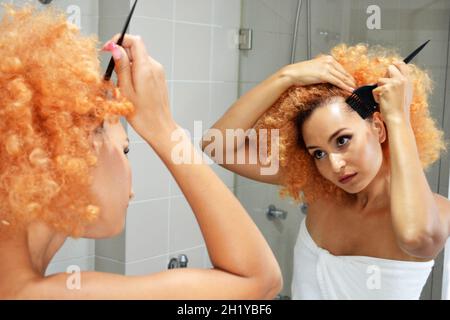 Die wunderschöne kaukasische Dame malte ihre Haarwurzeln zu Hause vor dem Badezimmerspiegel Stockfoto