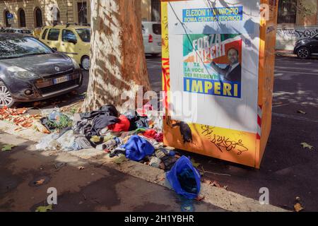 Mülltonne in Rom, Italien mit Plakat des Kandidaten für Kommunalwahlen. Müll verbreitete sich auf den Straßen der römischen Hauptstadt vor dem Müllcontainer und lag auf der Straße. Stockfoto