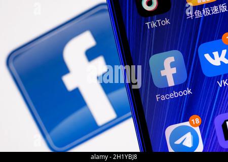 Das Symbol der Facebook-Anwendung für soziale Netzwerke unter anderem auf dem Smartphone-Bildschirm. Auf dem Hintergrund ist das Facebook-Logo zu sehen. Stockfoto