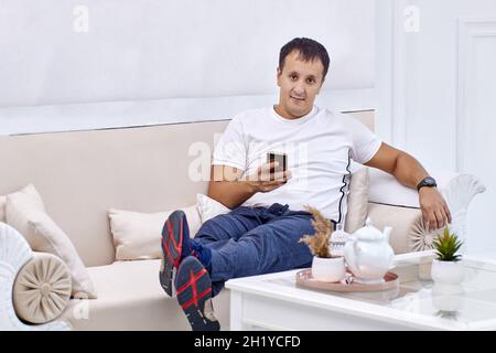 Gemischter Rennmensch liegt mit Mobiltelefon auf der Couch. Stockfoto