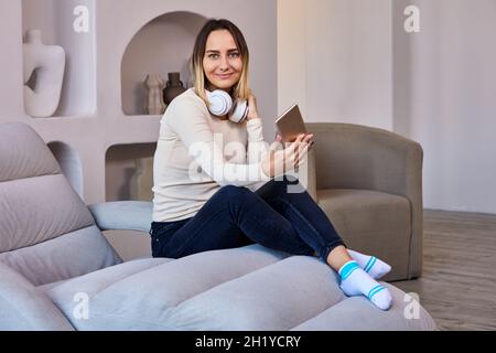 Lounge, in der die Frau auf dem Sofa und in Kopfhörern das Telefon hält. Stockfoto