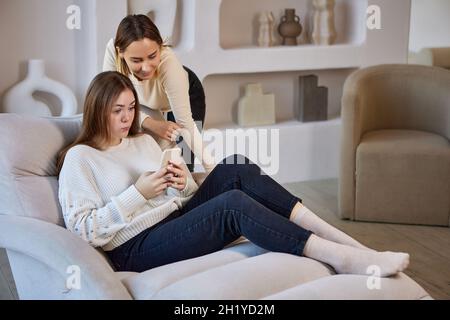 Chaiselongue mit zwei Schwestern mit Telefon auf dem Sofa. Stockfoto