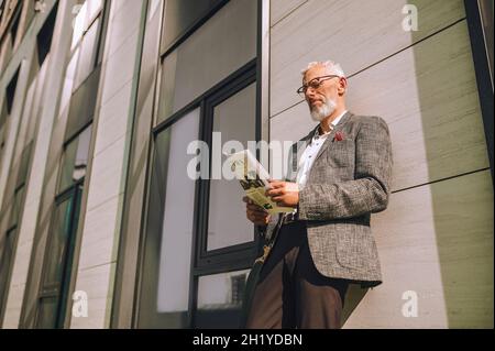 Ein grauhaariger Geschäftsmann, der eine Zeitung liest und dabei aussieht Stockfoto