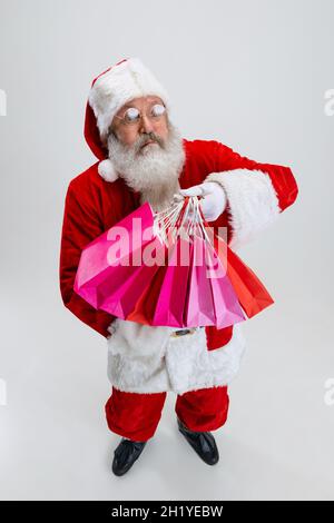 Ganzkörperportrait eines älteren Mannes, der ein Weihnachtsmann-Kostüm trägt und viele Einkaufspakete auf weißem Hintergrund hält. Vorbereitung auf den Urlaub Stockfoto
