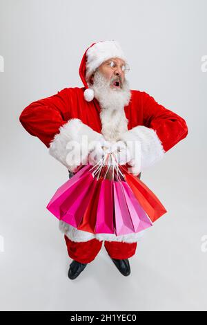 Ganzkörperportrait eines älteren Mannes, der ein Weihnachtsmann-Kostüm trägt und viele Einkaufspakete auf weißem Hintergrund hält. Vorbereitung auf den Urlaub Stockfoto