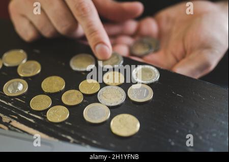 Geschäftsmann zählt Geld. Reiche männliche Hände halten und zählen Münzen verschiedener Euros auf dem Tisch vor einem Laptop Stockfoto