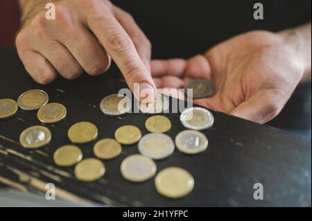 Geschäftsmann zählt Geld. Reiche männliche Hände halten und zählen Münzen verschiedener Euros auf dem Tisch vor einem Laptop Stockfoto