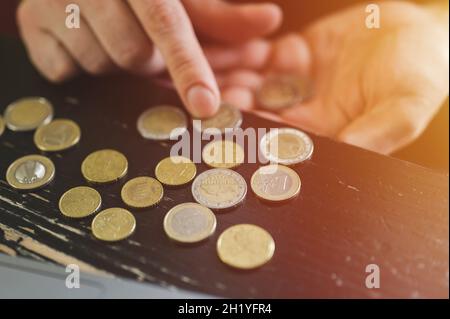 Geschäftsmann zählt Geld. Reiche männliche Hände halten und zählen Münzen verschiedener Euro auf dem Tisch vor einem Laptop. Fackel Stockfoto