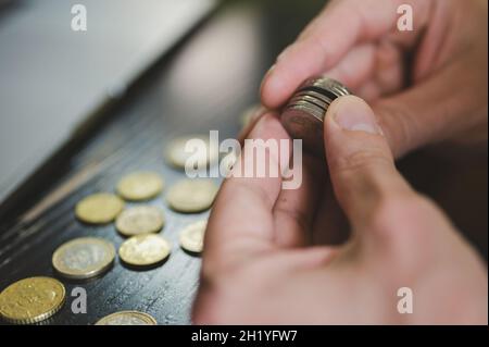 Geschäftsmann zählt Geld. Reiche männliche Hände halten und zählen Münzen verschiedener Euros auf dem Tisch vor einem Laptop Stockfoto