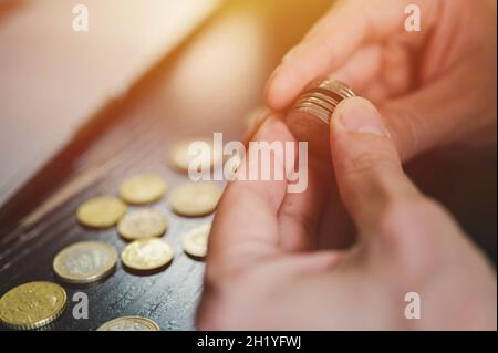 Geschäftsmann zählt Geld. Reiche männliche Hände halten und zählen Münzen verschiedener Euro auf dem Tisch vor einem Laptop. Fackel Stockfoto