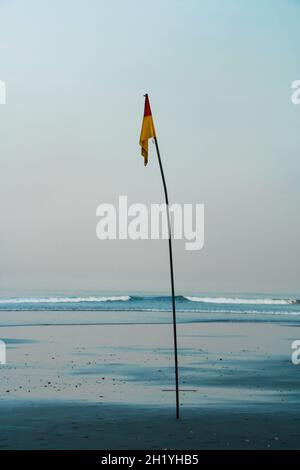 Warnflagge für die Sicherheit am Strand bei Sonnenaufgang mit Wasserspiegelung auf Sand und klarem blauen Himmel im Hintergrund. Keine Personen. Stockfoto