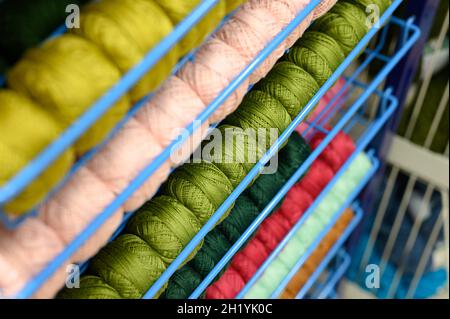 Reihen von Kugeln aus bunten Baumwollgarnfäden zum Stricken von blassrosa und grünen Farben auf den Regalen im Geschäft Stockfoto