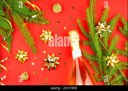 Der rote Weihnachtshintergrund des neuen Jahres mit einer Flasche Champagner, verziert mit Zweigen aus Fichte, Serpentin, Konfetti. Draufsicht Stockfoto