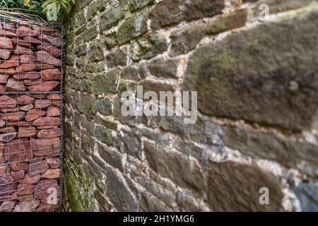 Altes Steinmauerwerk mit Kalkmörtelwand und einem neuen Stahlkäfig gabion, gefüllt mit eisenbefleckten lokalen Sandsteinen. . Stockfoto