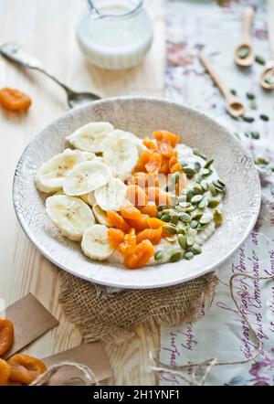 Hirseflocken aus Mandelmilch, Bananen, getrockneten Aprikosen und Kürbiskernen Stockfoto