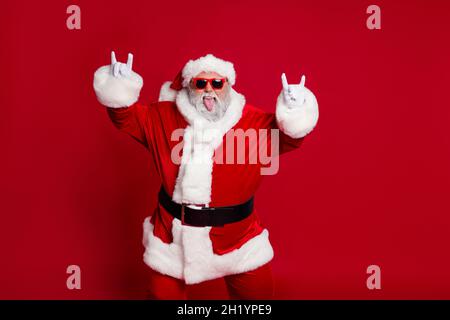 Portrait von attraktiven verrückt fröhlich kindisch Santa zeigt Horn Symbol mit Spaß isoliert über hellen roten Hintergrund Stockfoto