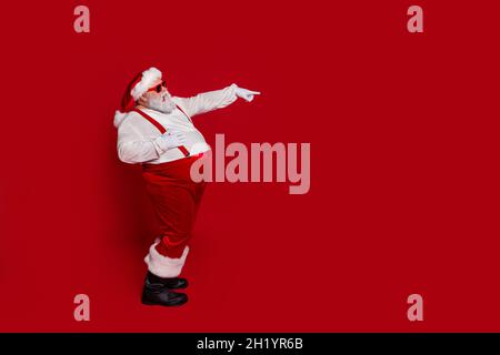 Profil Foto von funky Mann lachen direkte Finger leeren Raum Verkauf tragen weihnachtsmann Hut Kostüm isoliert roten Hintergrund Stockfoto
