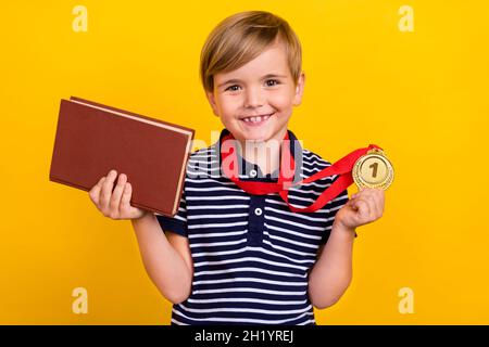 Foto Porträt kleiner Junge trägt goldene Medaille halten Buch isoliert lebendige gelbe Farbe Hintergrund Stockfoto