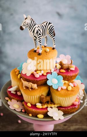 Cupcakes auf einem Kuchenständer, der mit Tierfiguren, Blumen und Süßigkeiten geschmückt ist Stockfoto