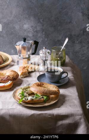 Frühstück mit hausgemachtem Bagel mit Sesamsamen, Frischkäse und Pesto-Sauce, Kaffee auf dem Tisch Stockfoto