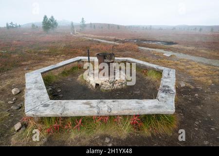 Offener Kamin mit Holzbänken in der finnischen Tundra. Nebliger Tag im Pahakuru-Gebiet, Pallas-Yllastunturi-Nationalpark, Finnland. Herbst in der Stockfoto