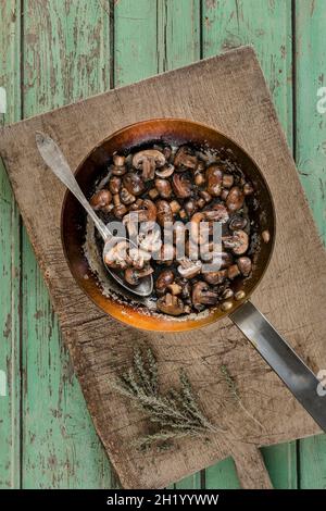 In Butter glasierter marsala-Wein und Thymian in einer rustikalen Bratpfanne mit Löffel auf einem hölzernen Schneidebrett braune Pilze anbraten Stockfoto