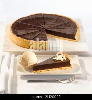 Schokoladentorte für zwölf Portionen in einem Konditoreikasten mit einer Kugel Vanilleeis Stockfoto