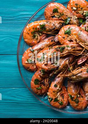 Gegrillte Garnelen werden auf einem Gericht mit Olivenöl, Petersilie und Knoblauch auf dunkelgrünem Holzboden serviert Stockfoto