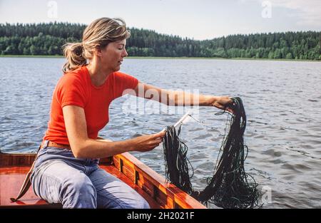 Junge Frau, die aus dem Boot mit Netz in einem schwedischen See angeln Stockfoto