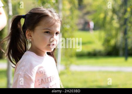 Kleines trauriges schönes Mädchen in einem rosa T-Shirt mit Zöpfen auf einem Spaziergang im Park Stockfoto