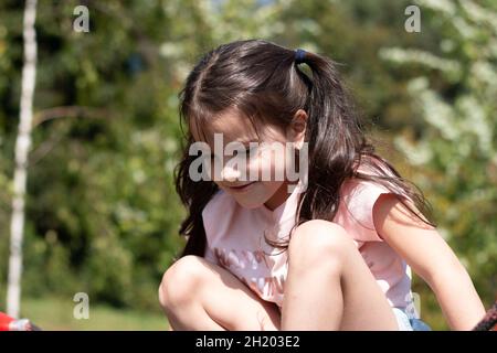 Kleines trauriges schönes Mädchen in einem rosa T-Shirt mit Zöpfen auf dem Spielplatz Stockfoto